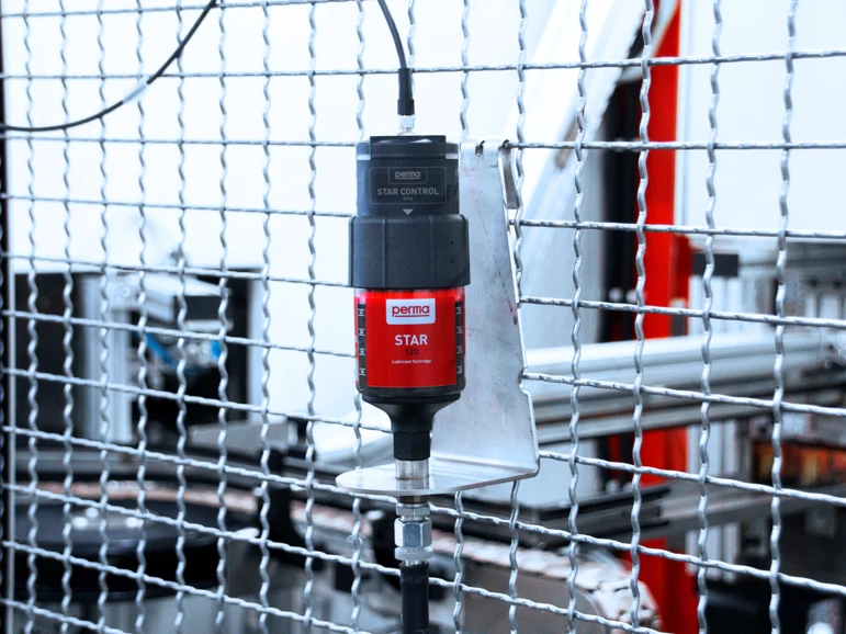 A perma STAR VARIO auto greaser installed on a cage protecting automotive manufacturing equipment